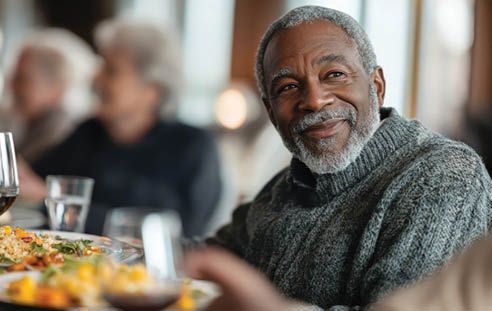 An older man is sitting at a table with a plate of food in front of him. AI generated content
