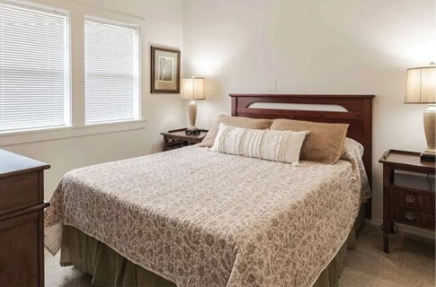 A bedroom with a bed, dresser, and lamp. The bed has a white comforter and a brown pillow. AI generated content