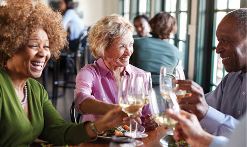 Three people are sitting at a table, enjoying a meal and drinking wine. They are smiling and having a good time. AI generated content